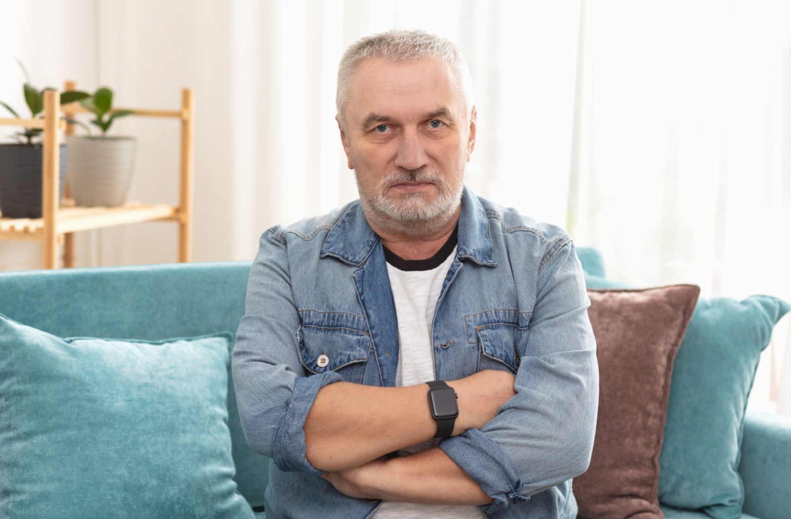 A negative older adult crosses his arms over his chest and stares into the camera with an unfriendly expression.