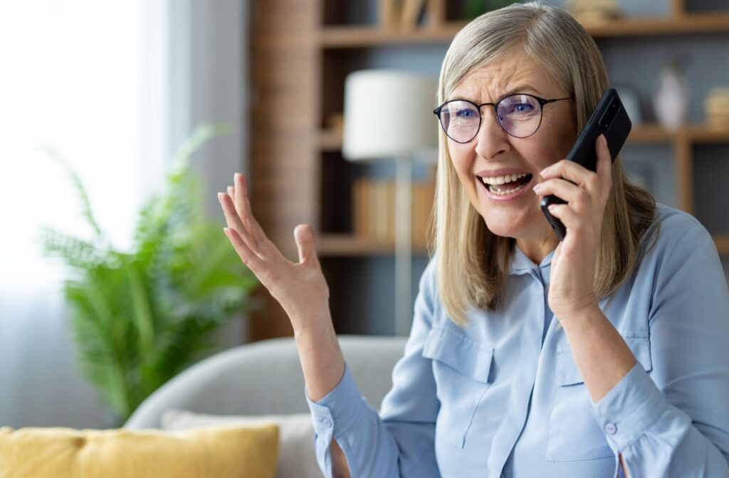 An elderly woman shouts into the phone, her right hand raised in frustration.