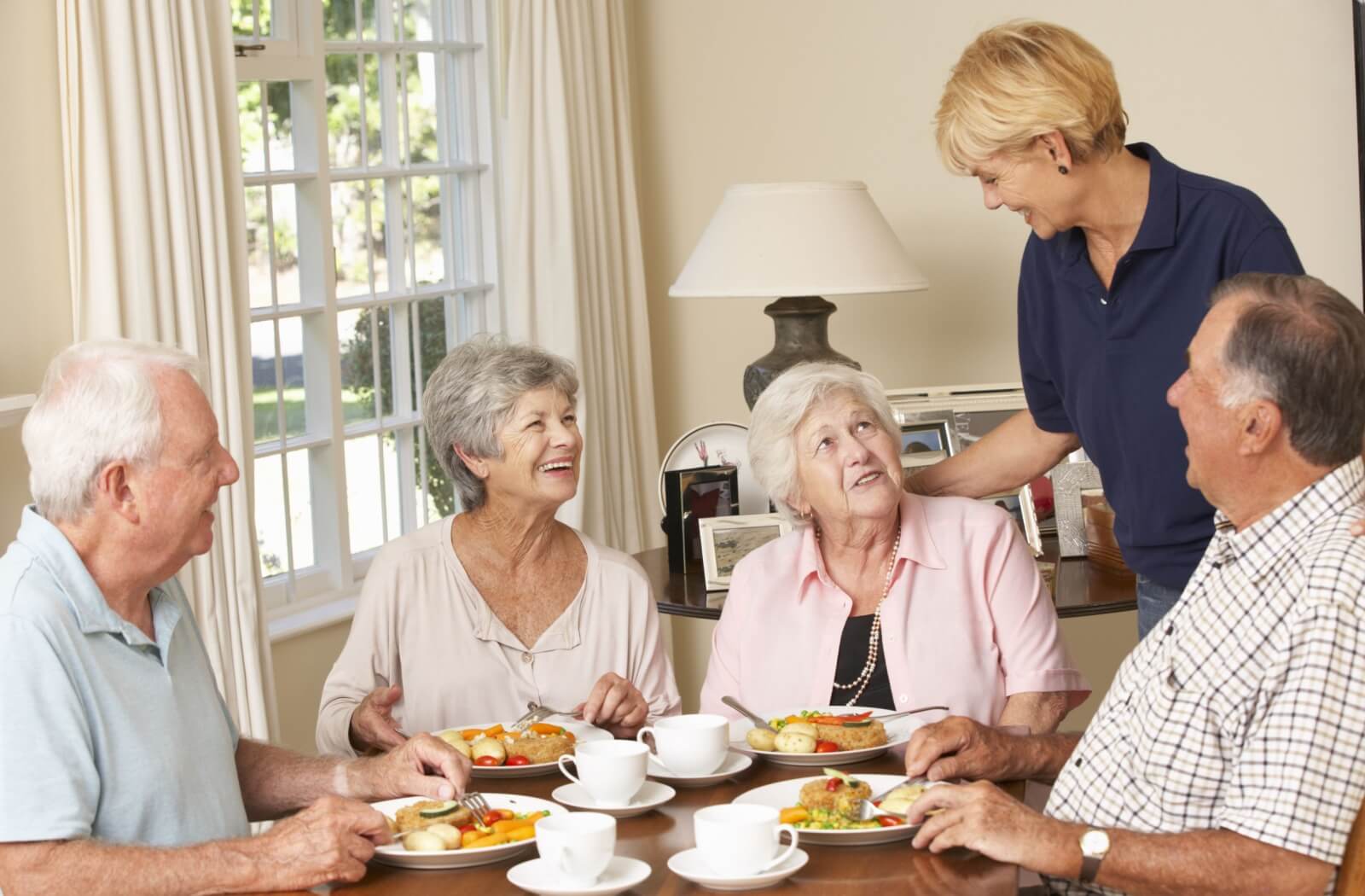 Group of older adults enjoying a meal together with a staff member during social dining in a senior living community.
