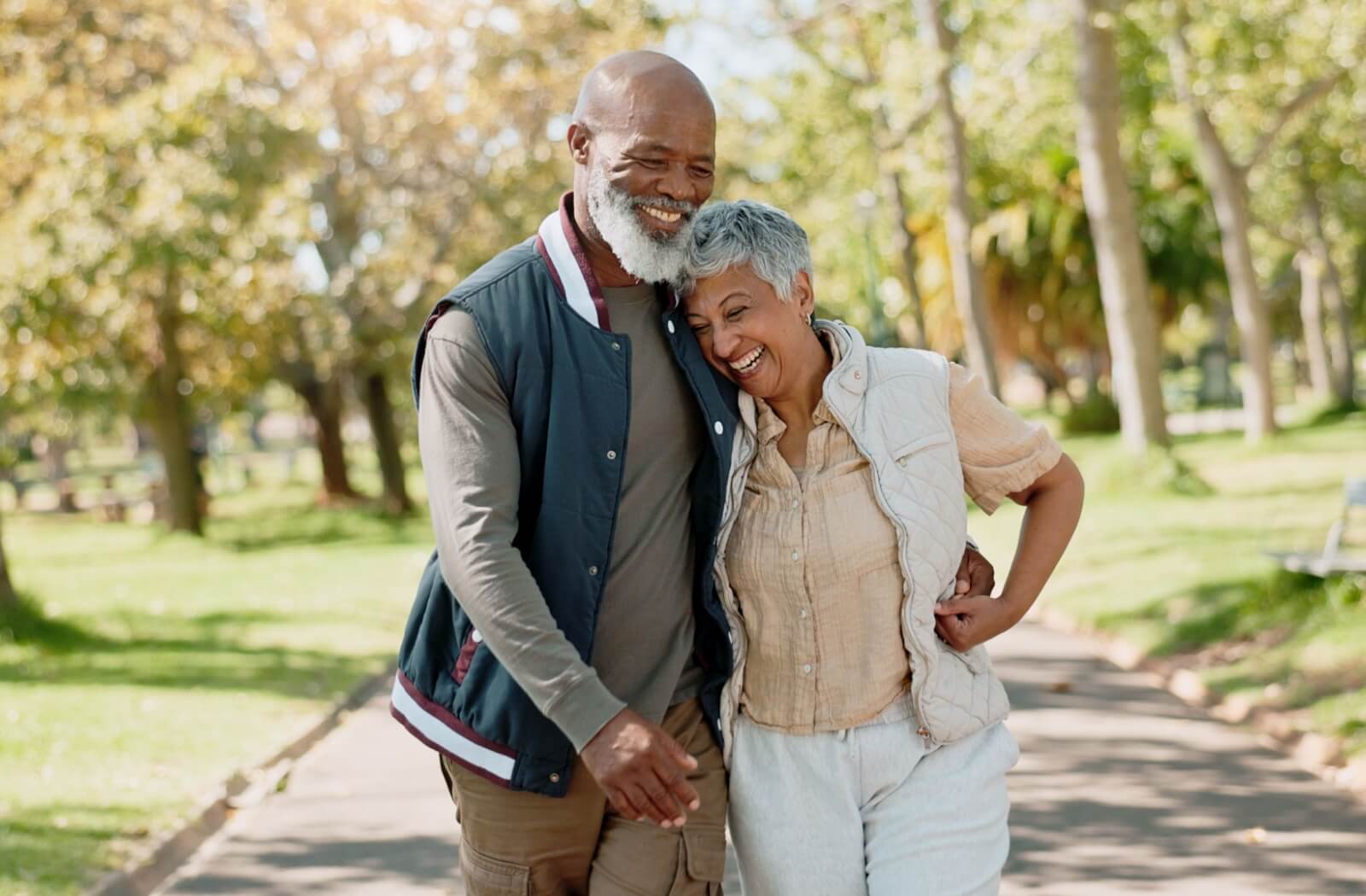 Senior couple laughing and walking arm in arm along a tree-lined path in a park
