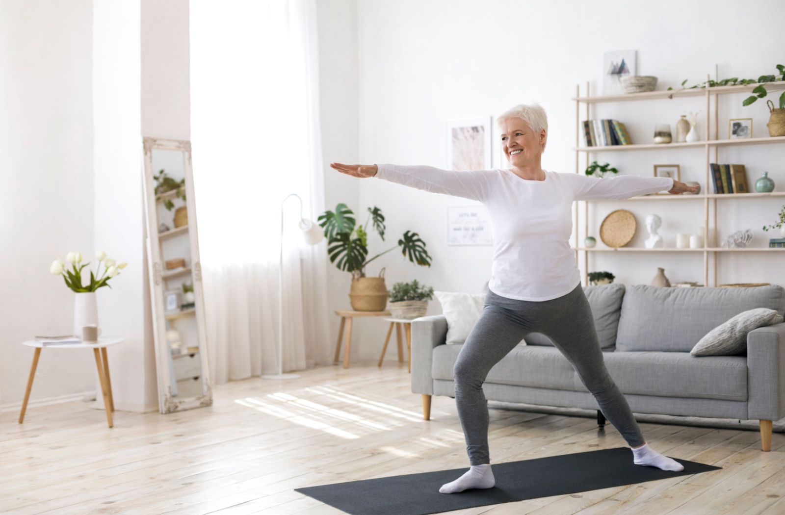 An older adult stretches their arms out during a yoga pose to improve their balance in their living room