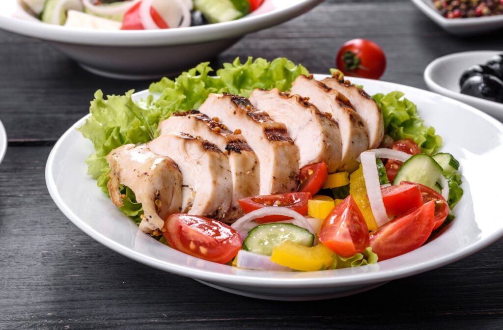 A close-up of a delicious plate of food with grilled and sliced chicken breast and freshly chopped salad on the side.